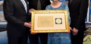 Image of small group of people, including Doctor Robert C. Nelson's wife, who is holding the Victor Stello Junior Award for Safety Leadership that was presented to her husband.